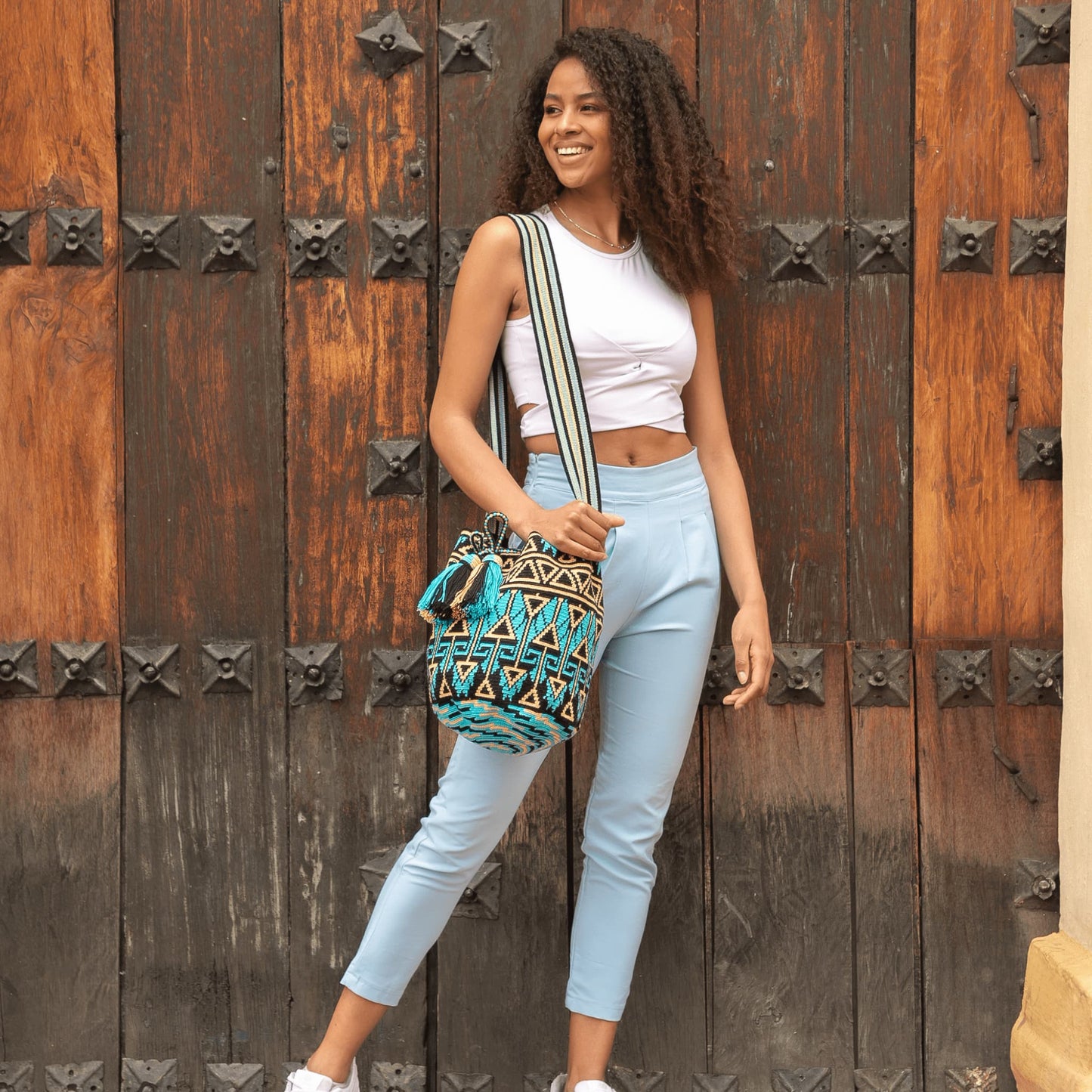 Handwoven Wayuu bag in black, blue, and beige with intricate geometric patterns. Features a matching small pouch for essentials, tassel details, and a sturdy strap.