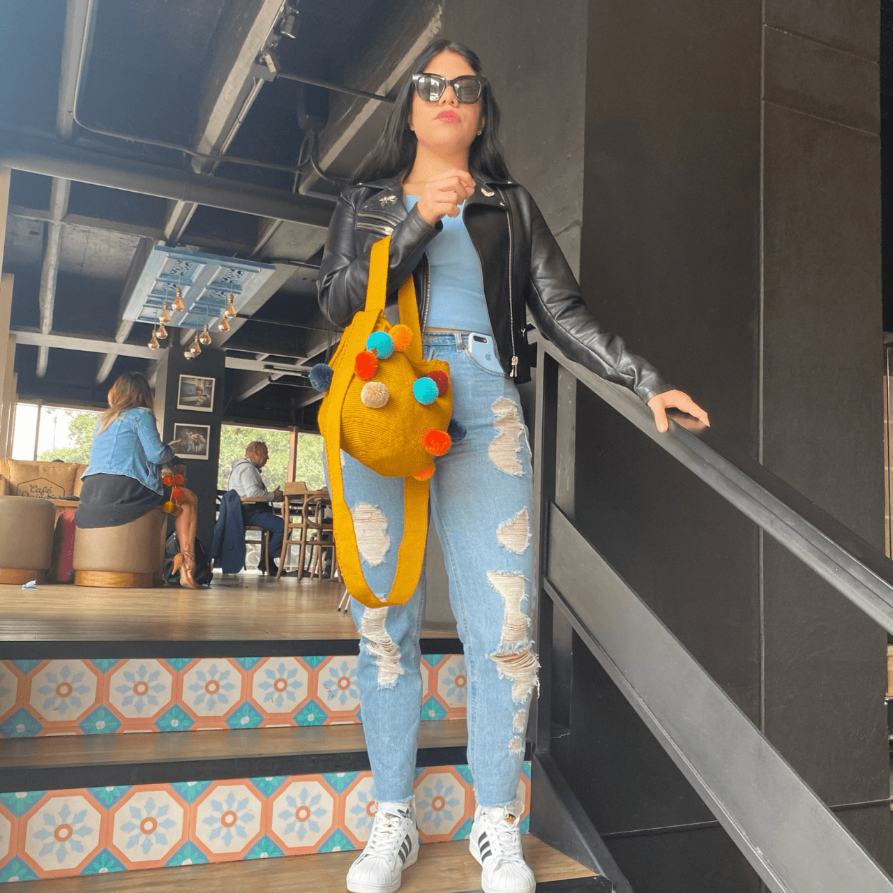 Koya crochet bag Medium in yellow color with vibrant pom poms, a stylish and eye-catching accessory.