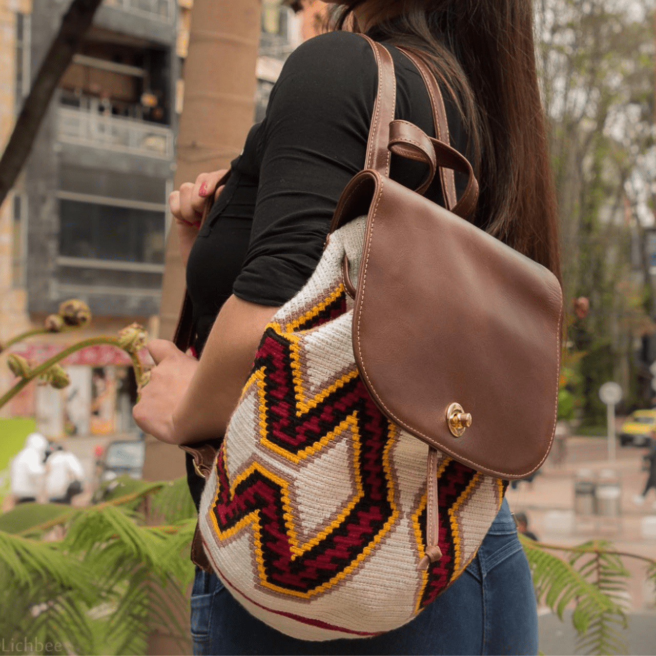 Nini backpack featuring a Wayuu body in a vibrant combination of white, red, yellow, and black, adorned with stylish accents in genuine leather. The backpack showcases a convenient side pocket and a secure double closing mechanism.