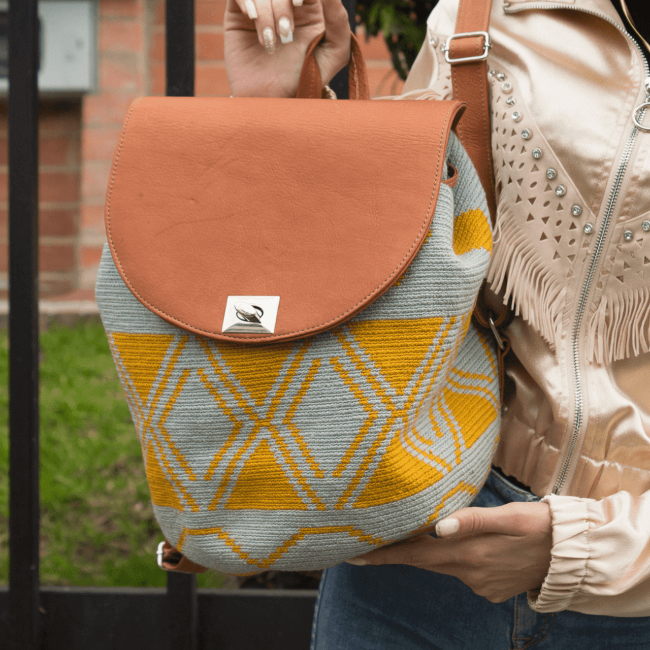 Taganga leather backpack featuring a stunning Wayuu pattern in a captivating blend of blue-gray and ochre colors. The design is accentuated with natural genuine leather, creating a beautiful contrast. This versatile bag is perfect for day outings or short trips, offering a lightweight and comfortable carrying experience.