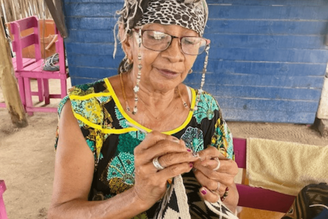 Experience the warmth and artistry of the Wayuu people. This image shows a Wayuu woman proudly displaying a handcrafted bag, a symbol of her cultural heritage and creative spirit.