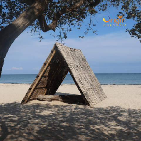 A rustic beach shelter made of dried palm leaves stands on the white sands of Mayapo beach, with the turquoise Caribbean Sea stretching to the horizon.