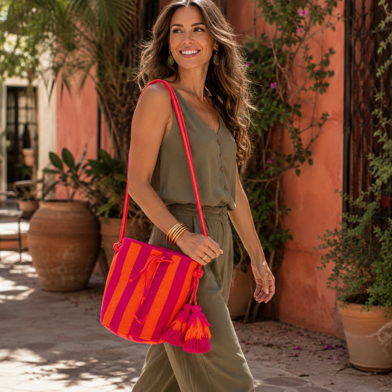 Handmade Wayuu bag with vibrant pink and orange stripes, long woven cord strap, and tassel detail.