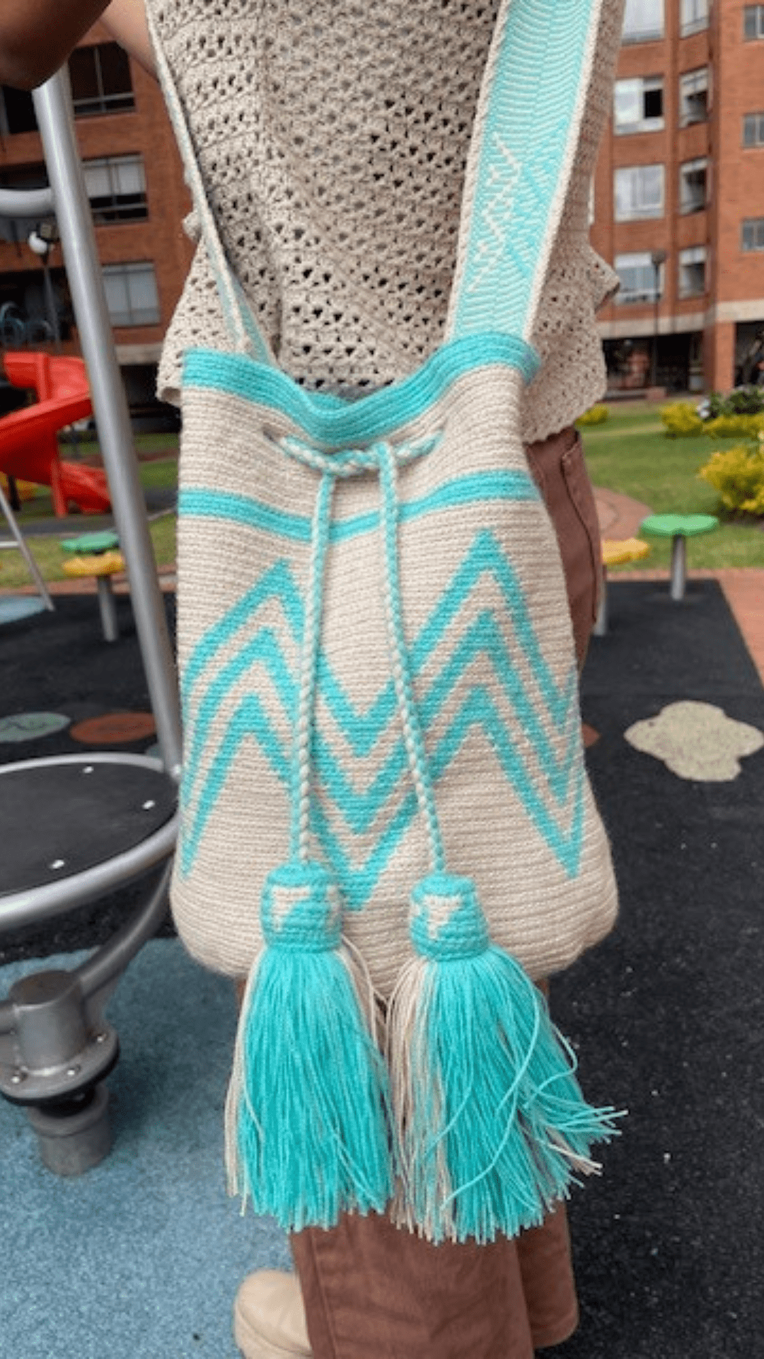 A simple yet captivating beige Wayuu bag adorned with aqua patterns, showcasing a minimalist design with intricate woven details.