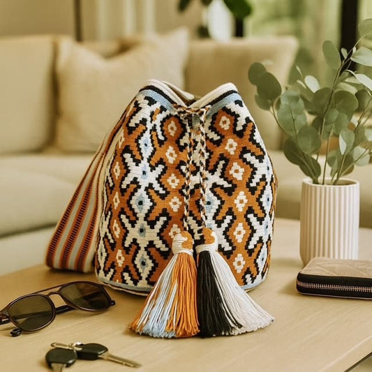 A handmade Wayuu bag featuring vibrant rusty orange, light blue, and black geometric patterns with a textured woven design.