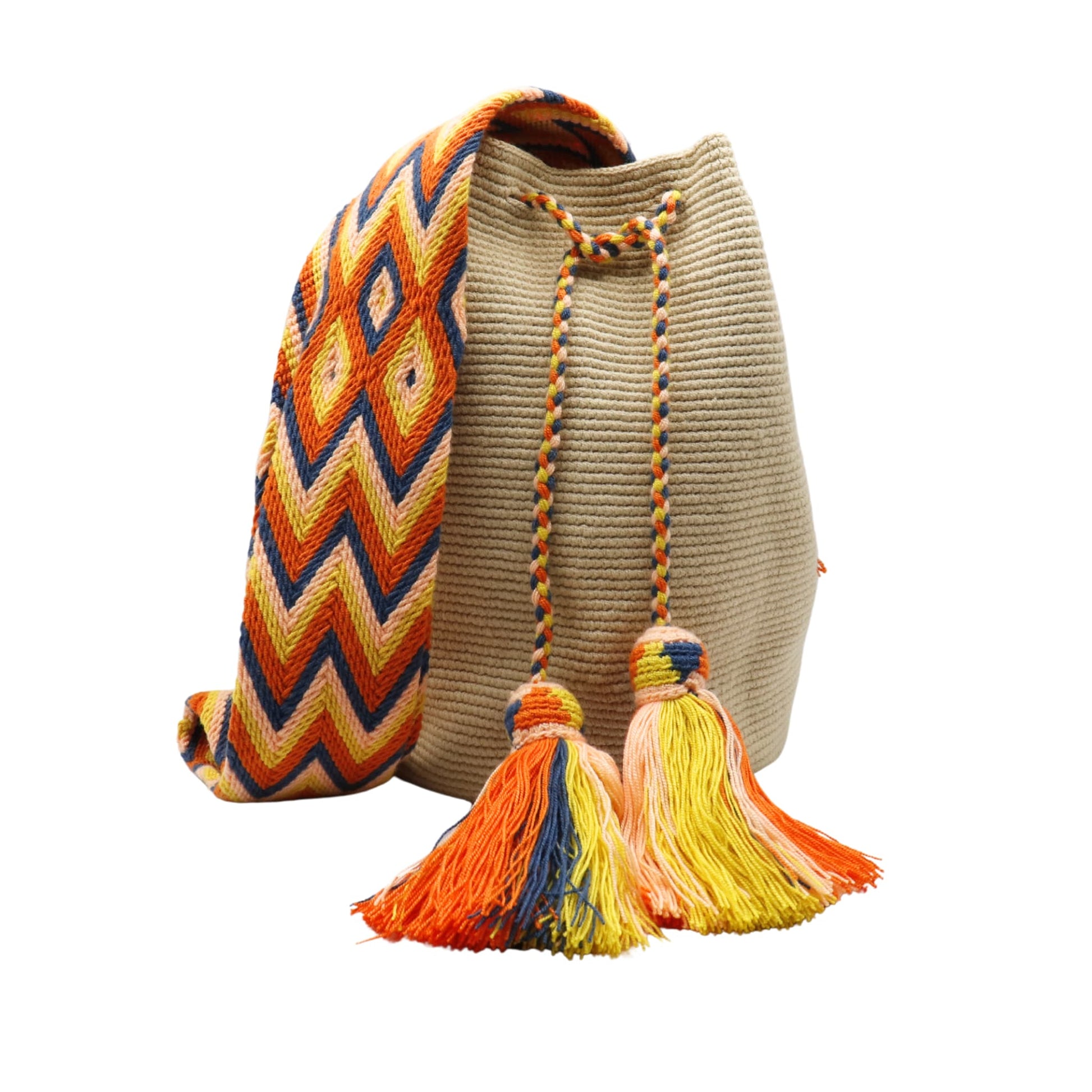 Beige handmade Wayuu bucket bag with a wide woven shoulder strap in orange, yellow, navy, and peach geometric chevron patterns. The bag features a braided drawstring closure with two large multicolored tassels and a soft, textured crochet body.