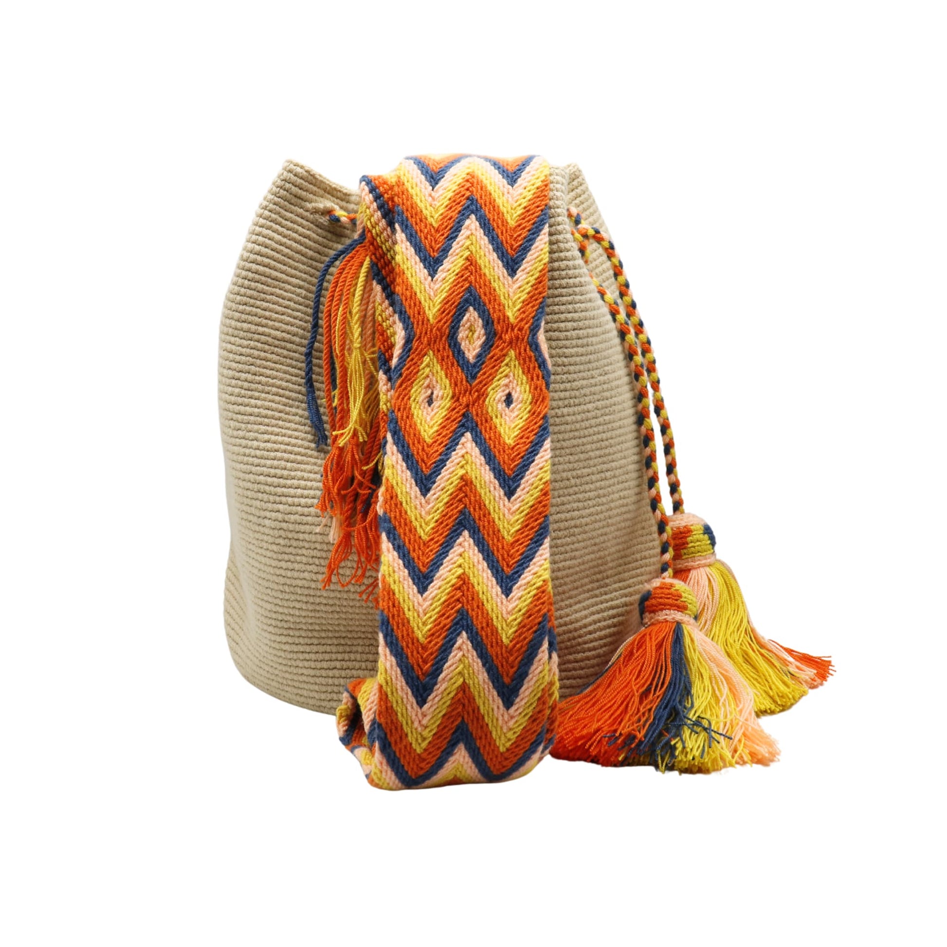 Beige handmade Wayuu bucket bag with a wide woven shoulder strap in orange, yellow, navy, and peach geometric chevron patterns. The bag features a braided drawstring closure with two large multicolored tassels and a soft, textured crochet body.