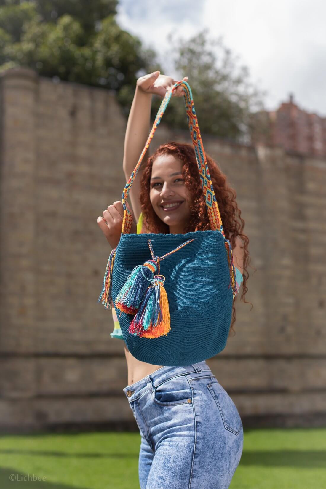 Handwoven Wayuu bag in vibrant cobalt blue with a colorful braided strap and tassels in shades of turquoise, orange, and yellow. A unique artisan piece from Colombia.